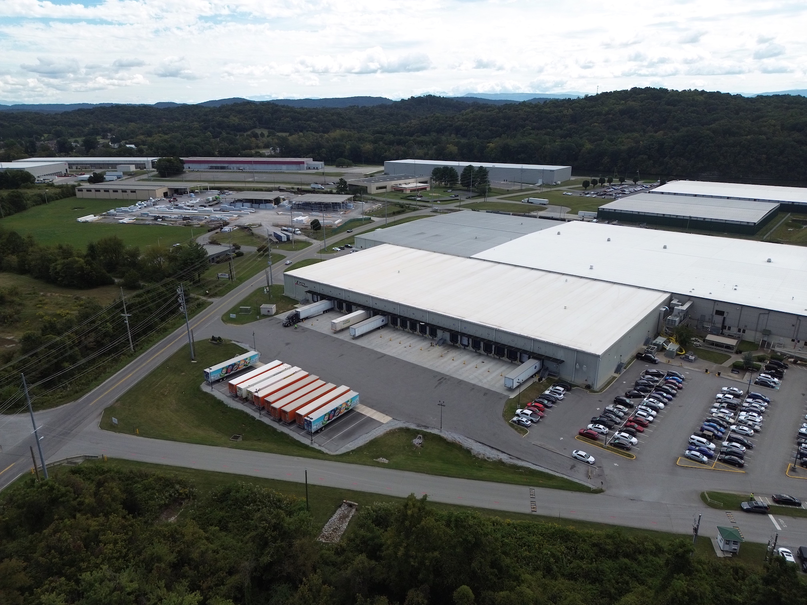 aerial image of a warehouse with semi-trucks and parking lot, trees, and sky in background